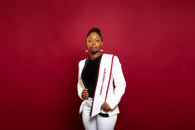 A determined looking TWU student portrait on a maroon background and dressed professionally and with a graduation stole that says 