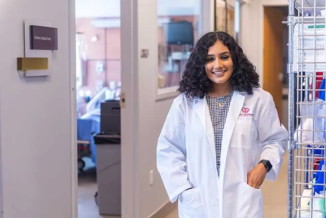 A TWU htudent in a healthcare office setting and wearing a labcoat.