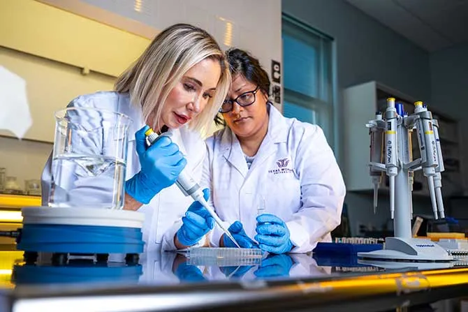 Two women wearing full PPE in a science lab setting.