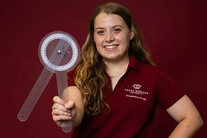 A TWU OT student stands for a portrait and holds an OT tool.