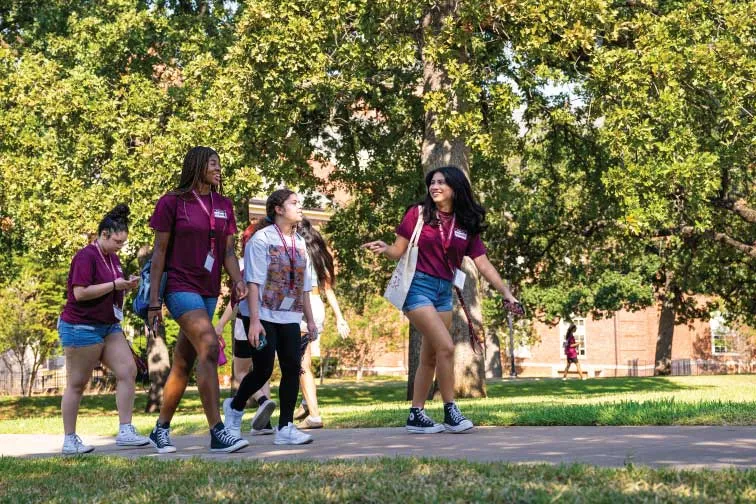 TWU Students smile and walk across the Denton campus on a sunny day.