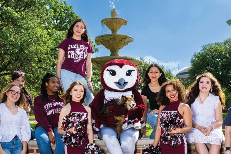 Oakley sits around the fountain with a diverse group of students all dressed in maroon and white.