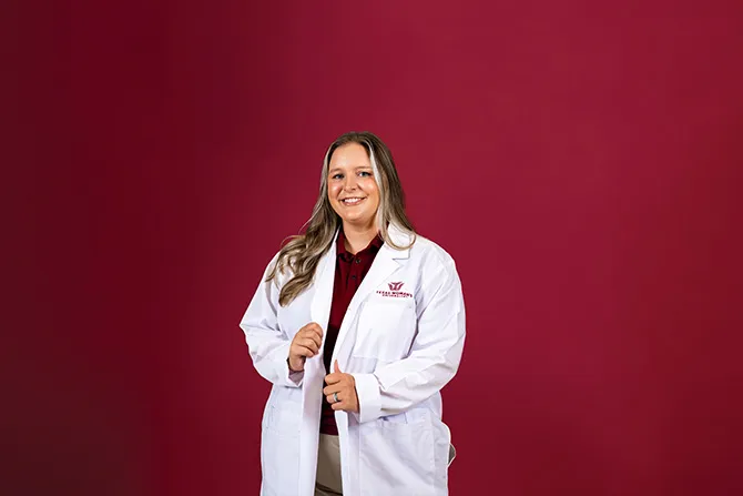 A determined looking TWU student portrait on a maroon background and dressed in healthcare labcoat.