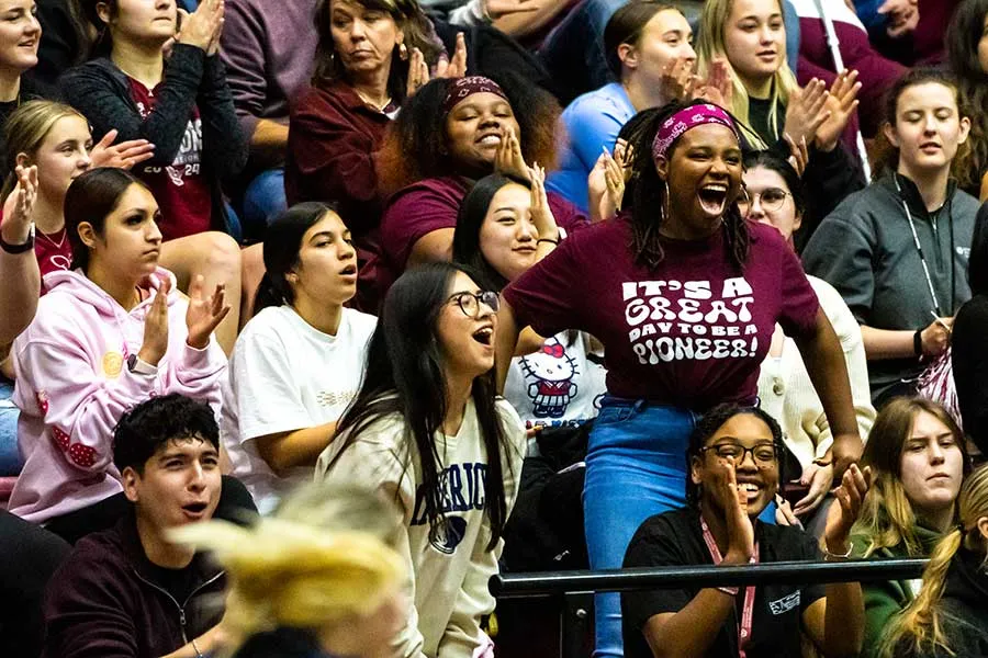 Filled stands in the Basketball arena and one cheering student stands out in the crowd.