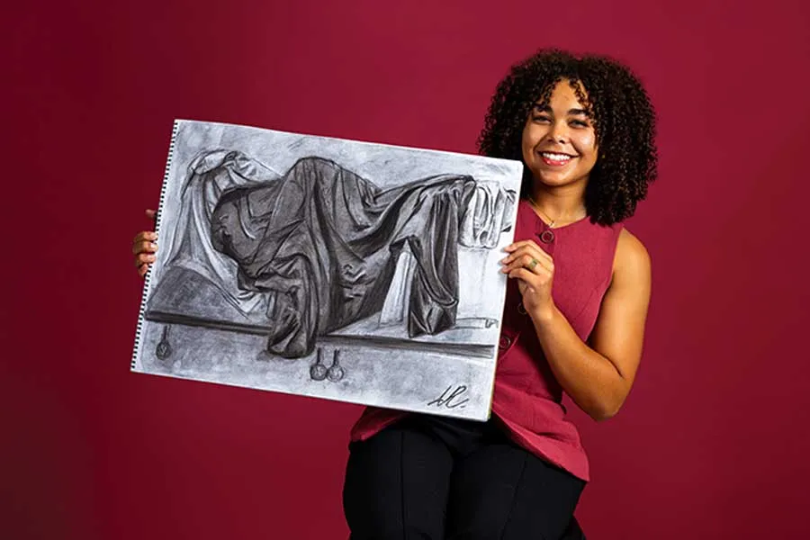 A dramatic portrait of a TWU student in business professional attire and holding a piece of her own artwork.
