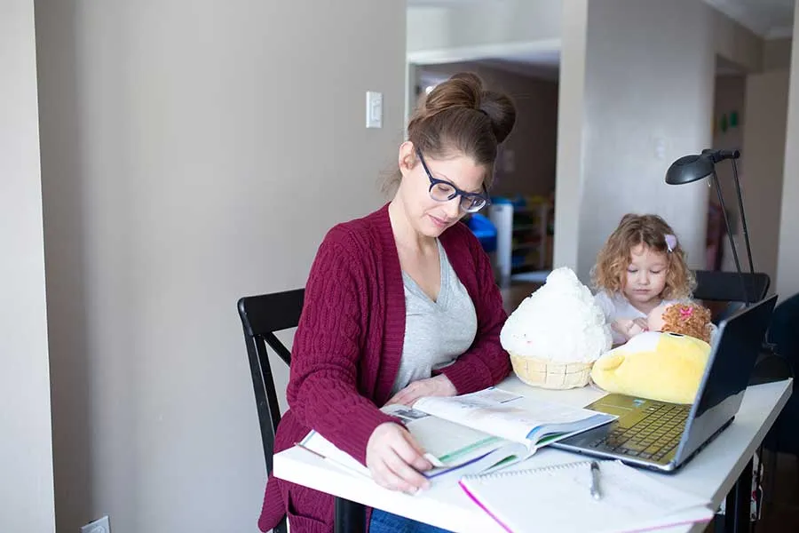 A woman works on her own studies while her daughter works next to her.