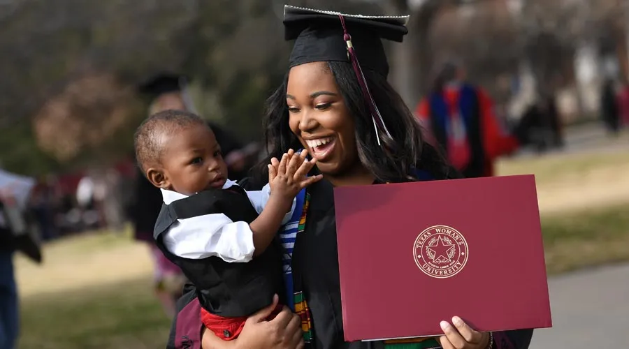 A graduate with her diploma holding her child 