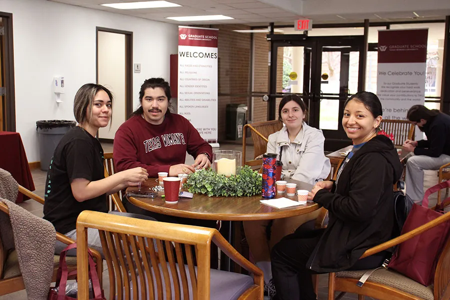A group of graduate students sit together at a table with snacks outside the TWU Graduate School offices
