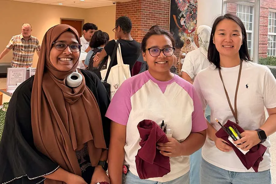 Three graduate students posing with smiles in crowd of other students
