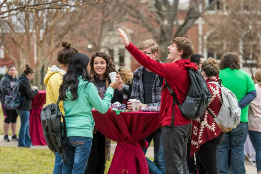 A group of students at a table in Pioneer Circle. One student waves to a friend off camera.