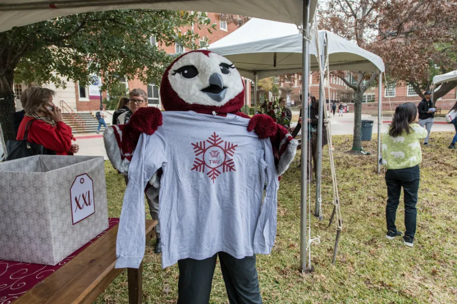 Oakley holding up a long-sleeve gray shirt with the TWU logo inside of a snowflake on it.