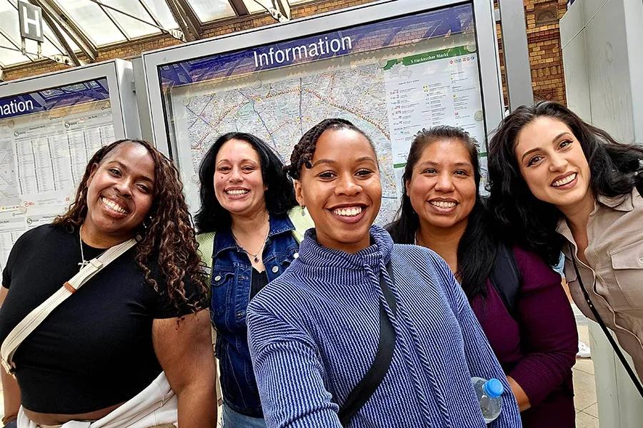 a women in a blue shirt stands in the middle between four women in front of a bus map