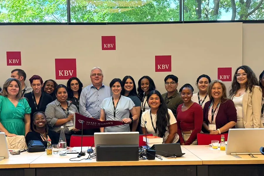 a group of MHA students in professional attire stand behind a long desk