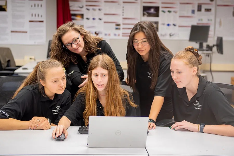 a kinesiology student works on computer while two students stand behind her and two more sit next to her