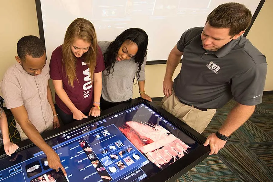 three students look at horizontal tv screen next to faculty member