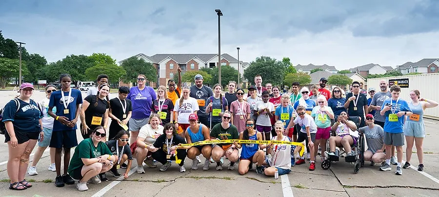 coaches and campers from camp abilities sit and stand in three rows in a parking lot.