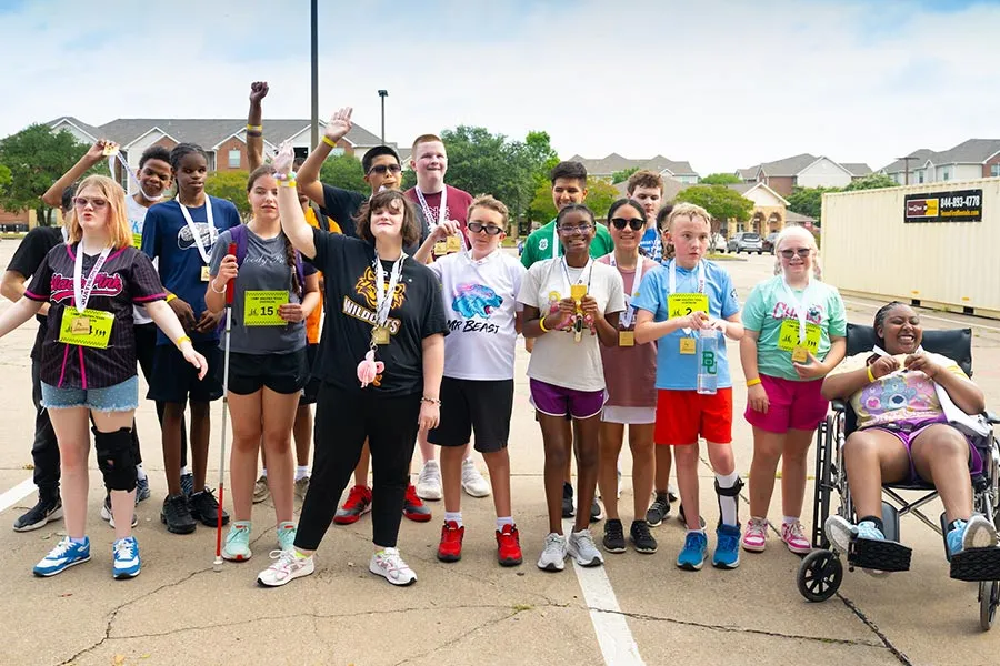 17 young campers stand in two rows in a parking lot with medals around their necks