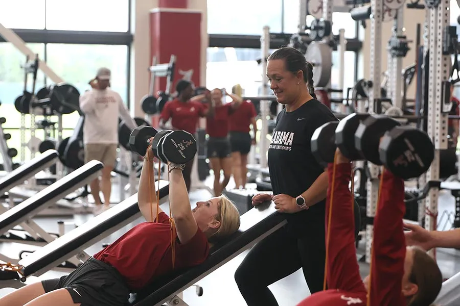 Michelle Diltz stands behind an athlete in red shirt pressing dumbells
