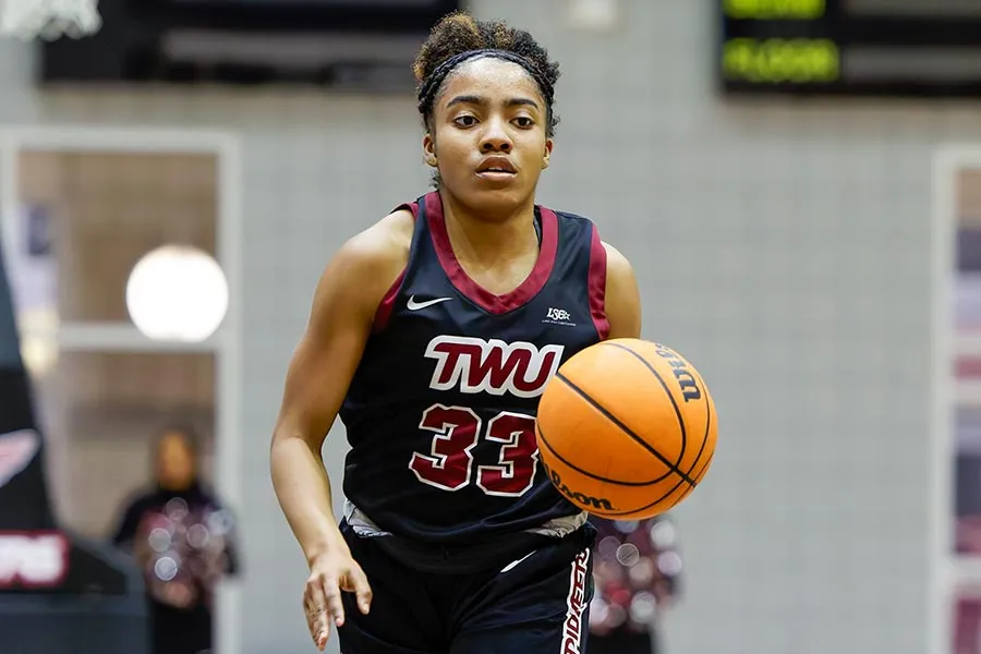 TWU basketball player in black uniform dribbles the ball in gym