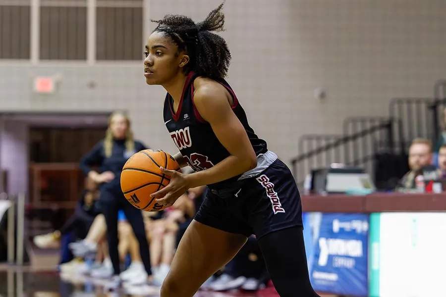 TWU basketball player in black uniform holds the ball in gym