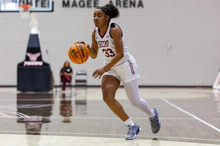 TWU basketball player in white uniform dribbles the ball in gym