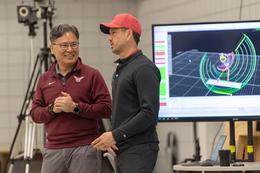 TWU professor Young-Hoo Kwon, PhD stands next to former student Chris Como and a large monitor