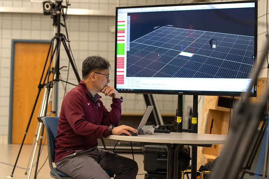 Dr. Kwon sits at table looking at a computer with a large monitor in the background