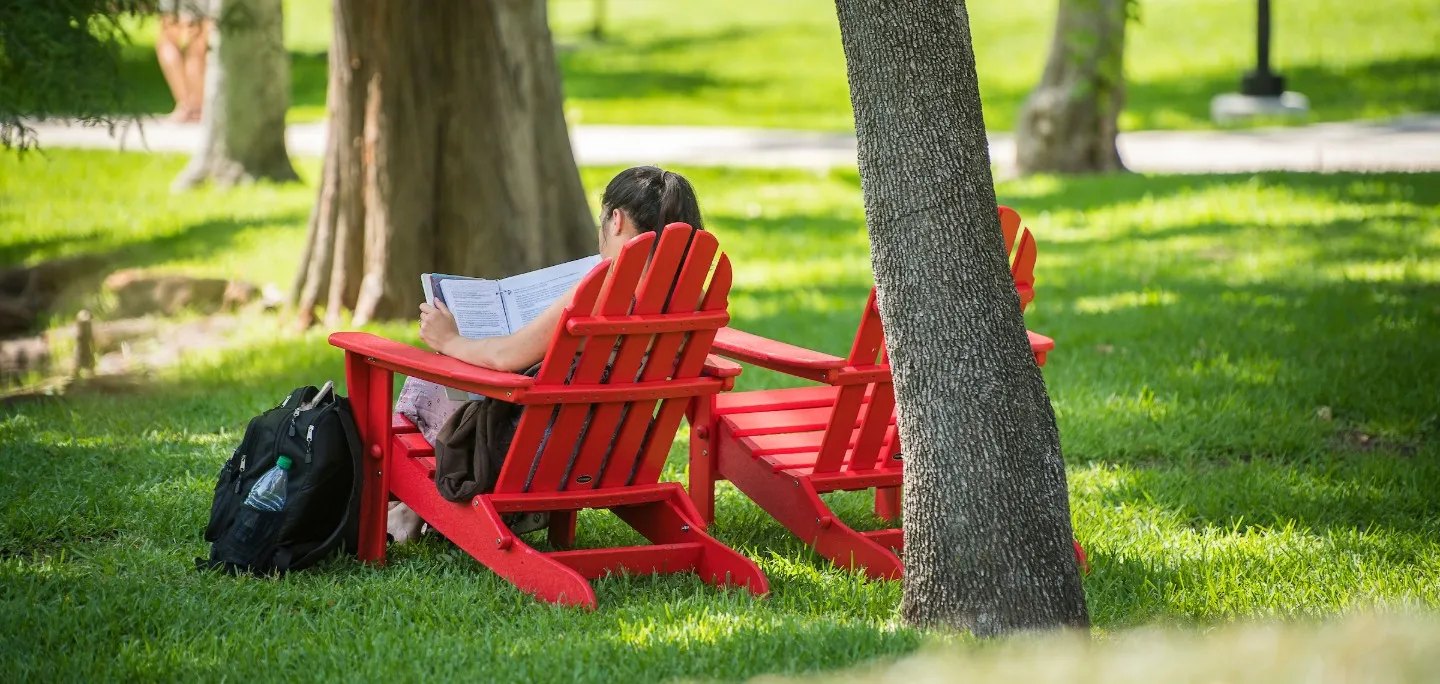 Girl relaxing in red chair under trees