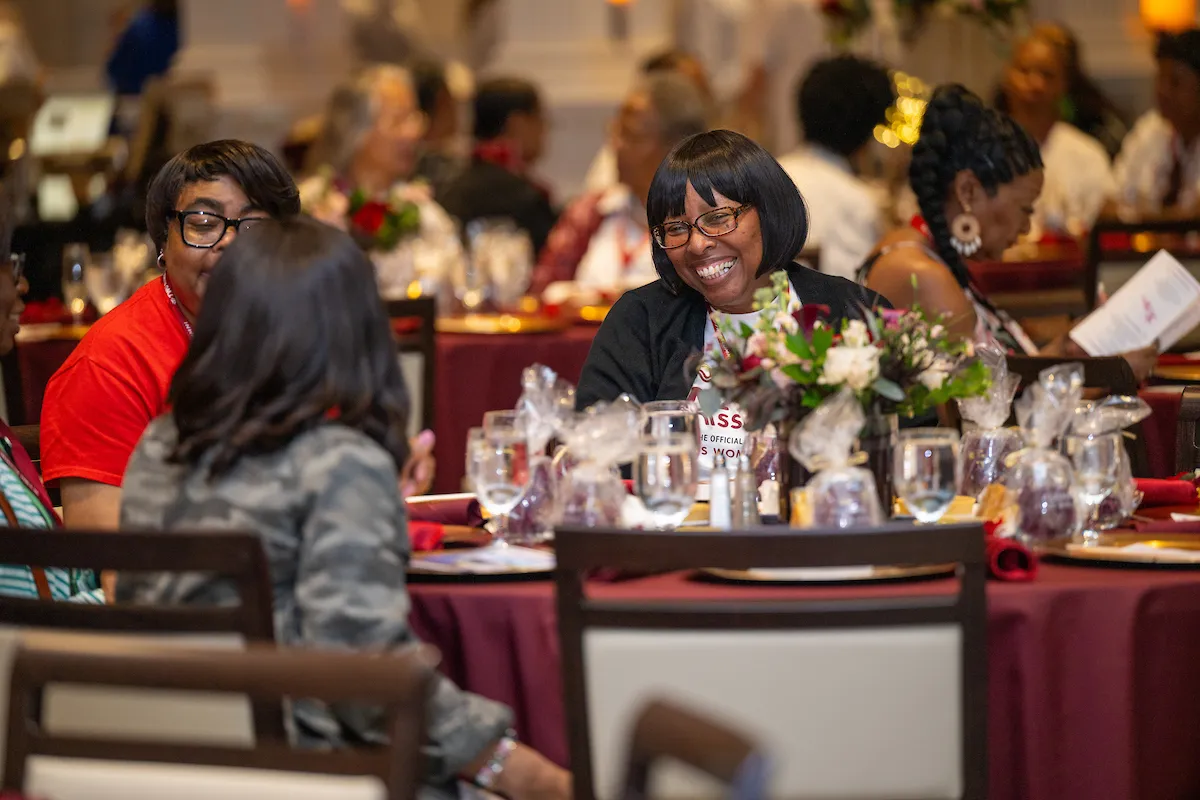 Three alumni sit smiling around a table at the reunion dinner.