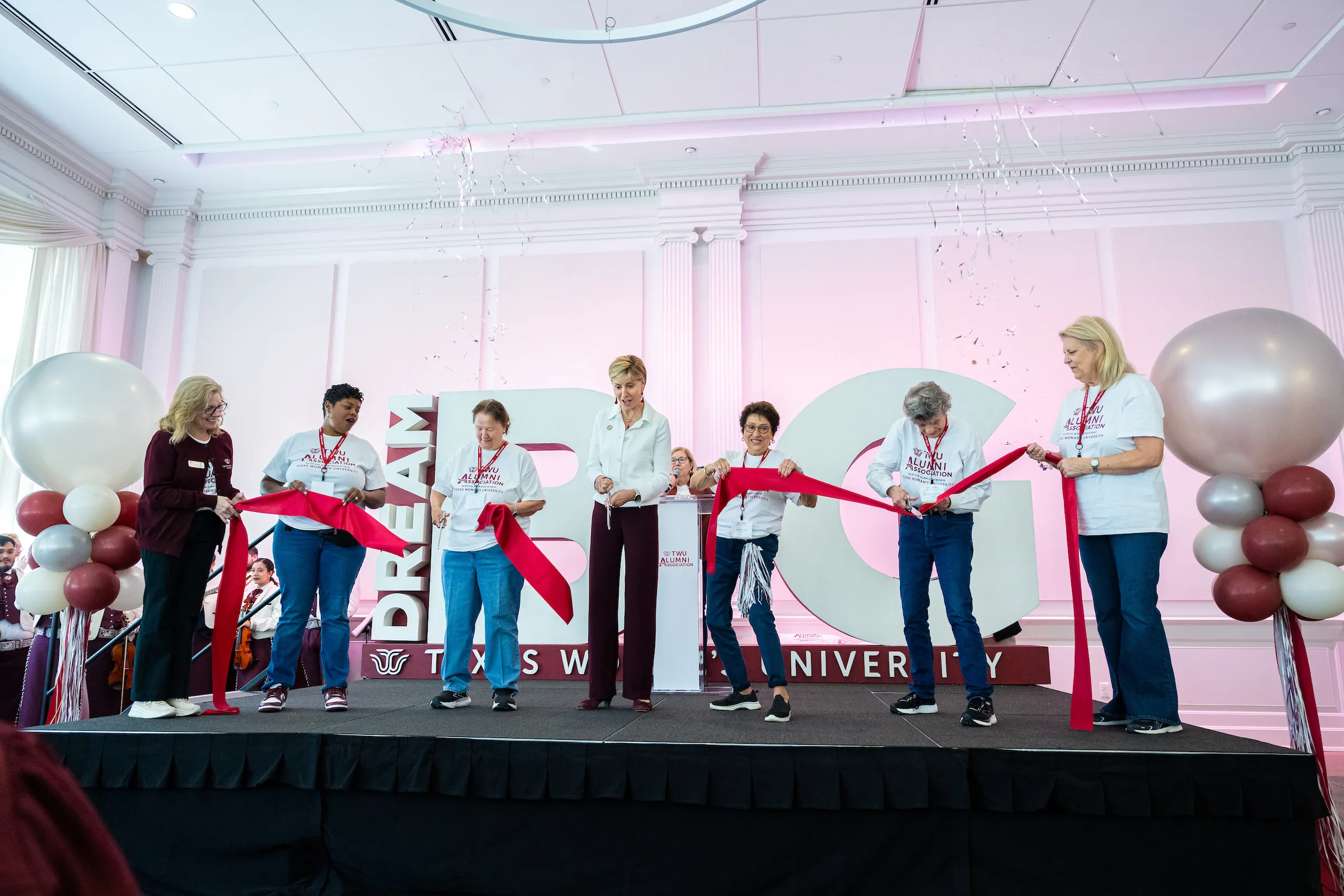 The chancellor and several alumni cut a big red ribbon at the Alumni Association launch celebration at Homecoming.