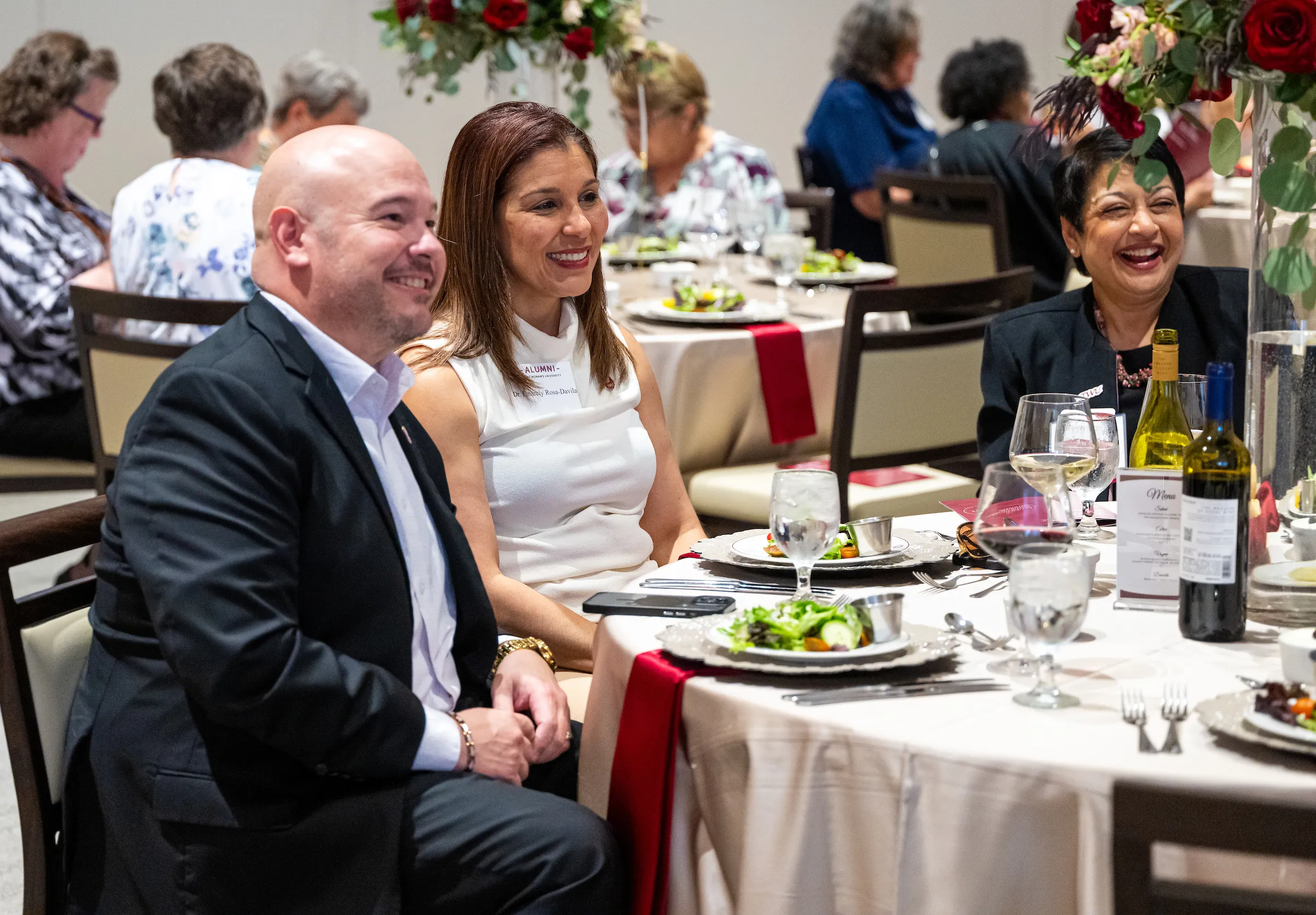 Attendees of the awards dinner sit smiling at a formally-set table as they chat and watch the presentations.