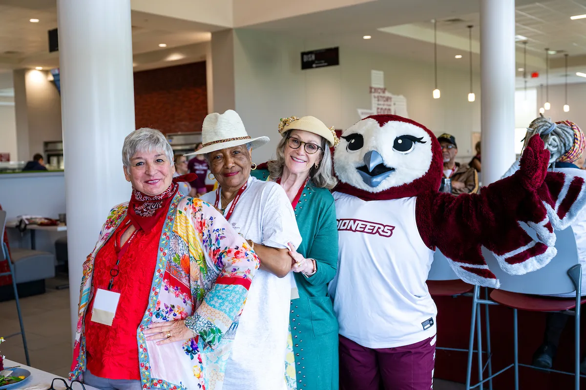 Three alumni pose smiling with Oakley at the Homecoming howdy lunch.