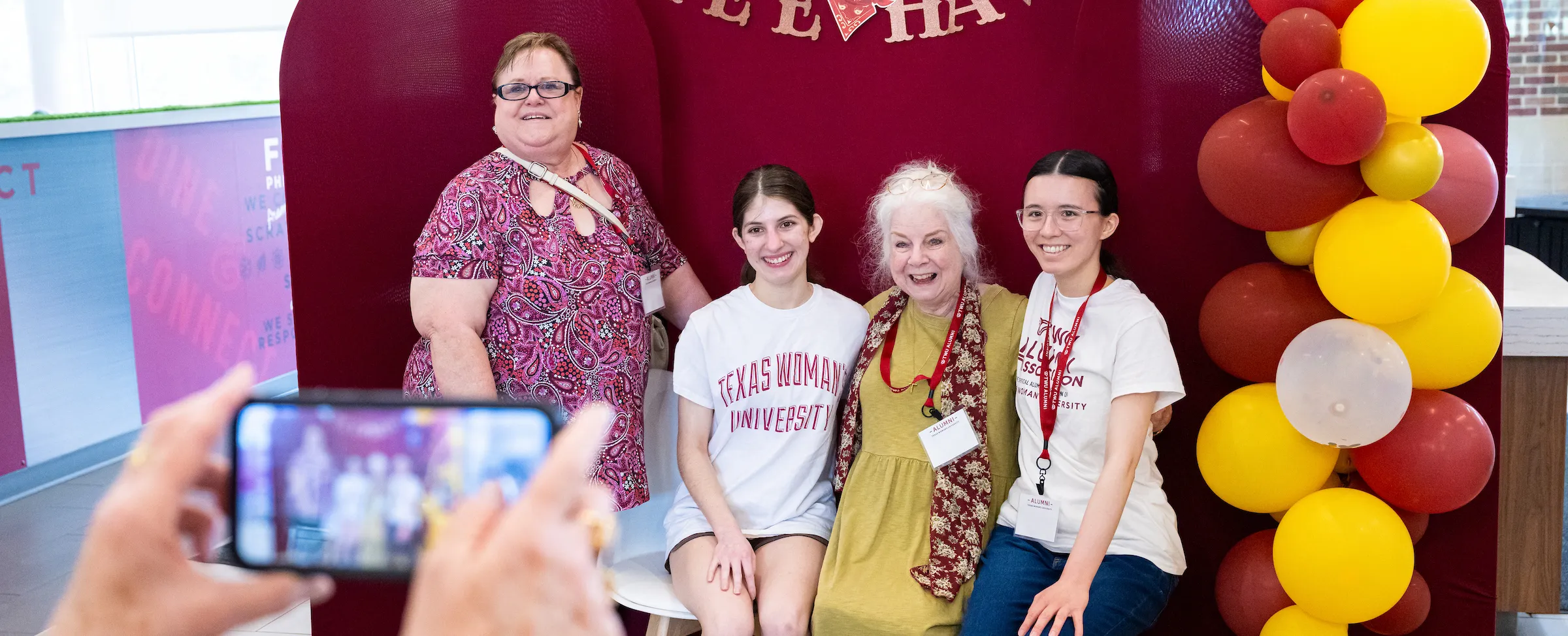 Four alumni of different generations pose for a picture in front of a maroon backdrop.
