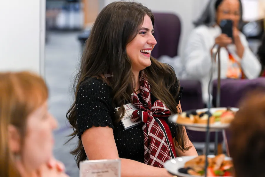 An attendee laughs during the Chancellor's talk, surrounded by pastries on tiered displays.