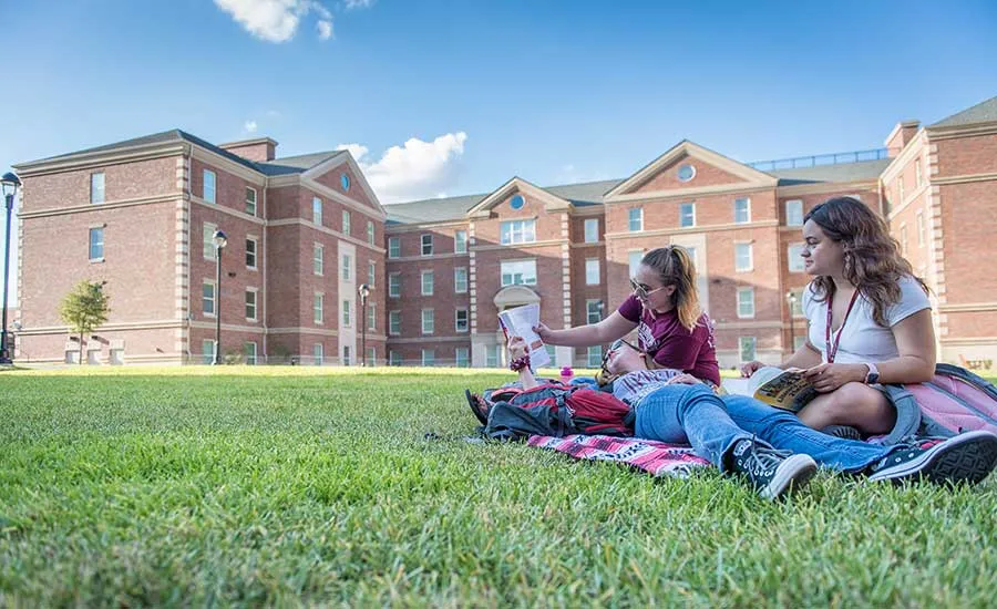 A group of three TWU students lounging on the grass at Parliament Village and studying.