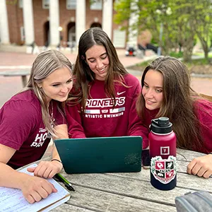 Three TWU Honors students look at a laptop just outside the Blagg-Huey Library on the Denton campus