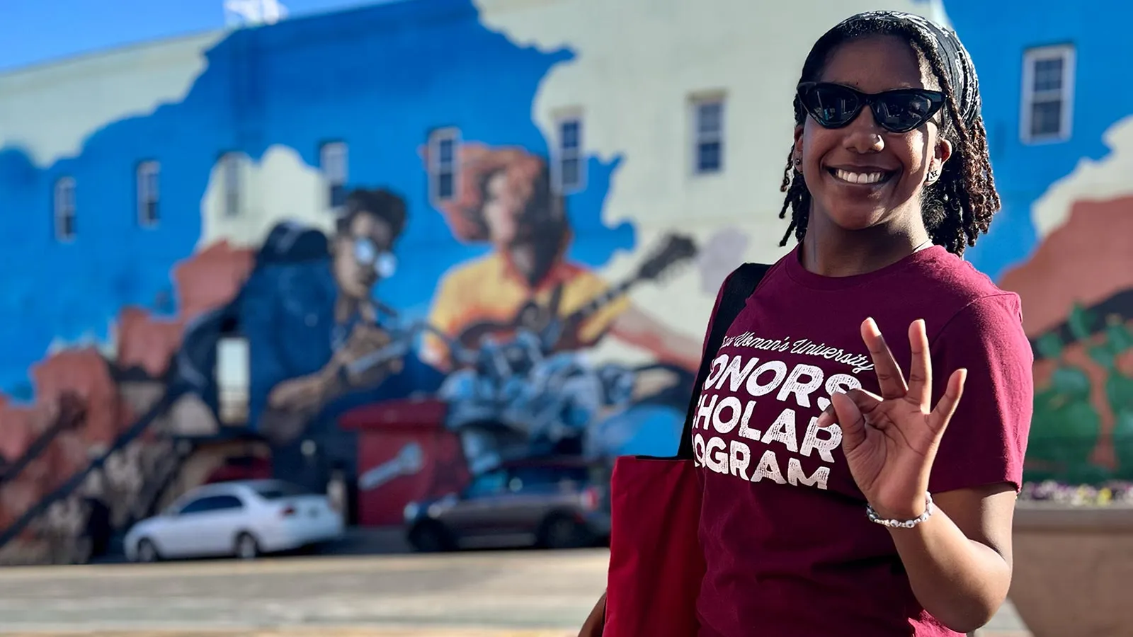 A TWU Honors student stands in front of a large building mural
