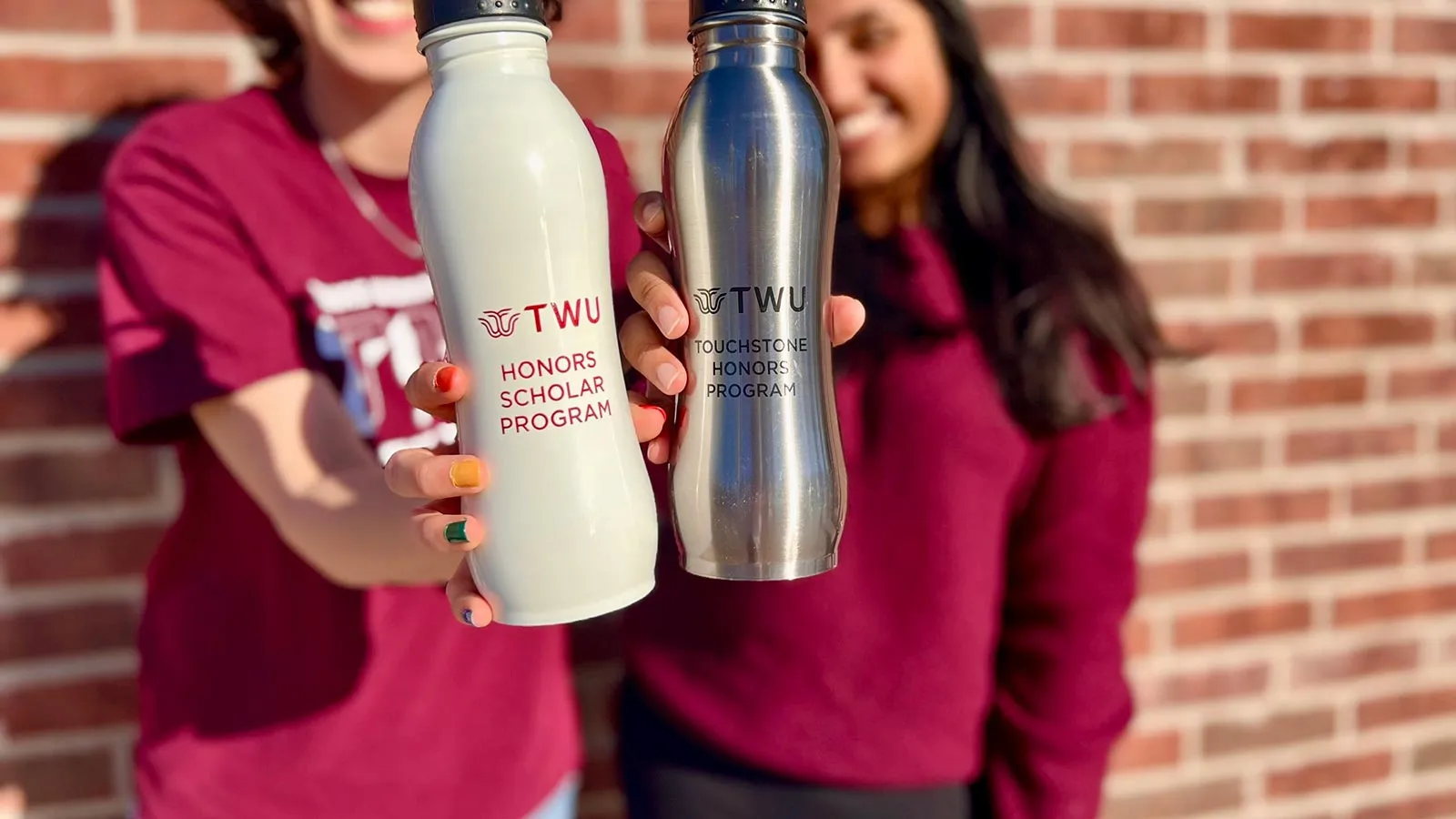 Two Honors students hold out water bottles with the TWU Honors Program logo on them