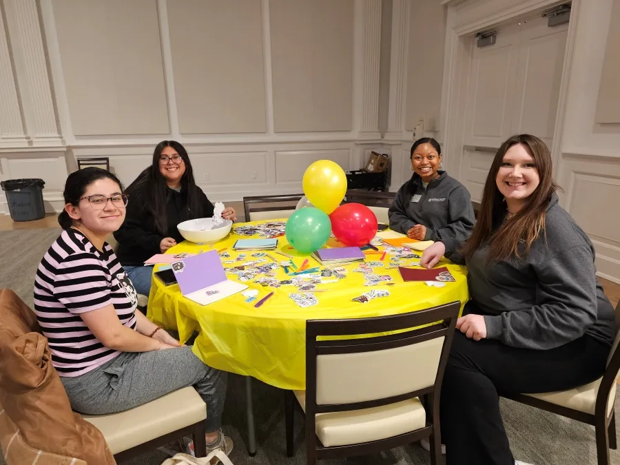 Students smile at camera as they sit around a table