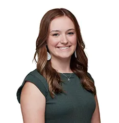 Girl in muted green shirt smiling in front of white background.