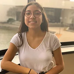 Girl with glasses smiles in front of a window