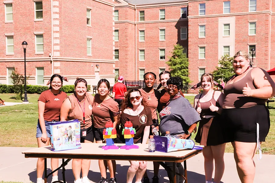 Students stand around a table with block on it outside on a sunny day
