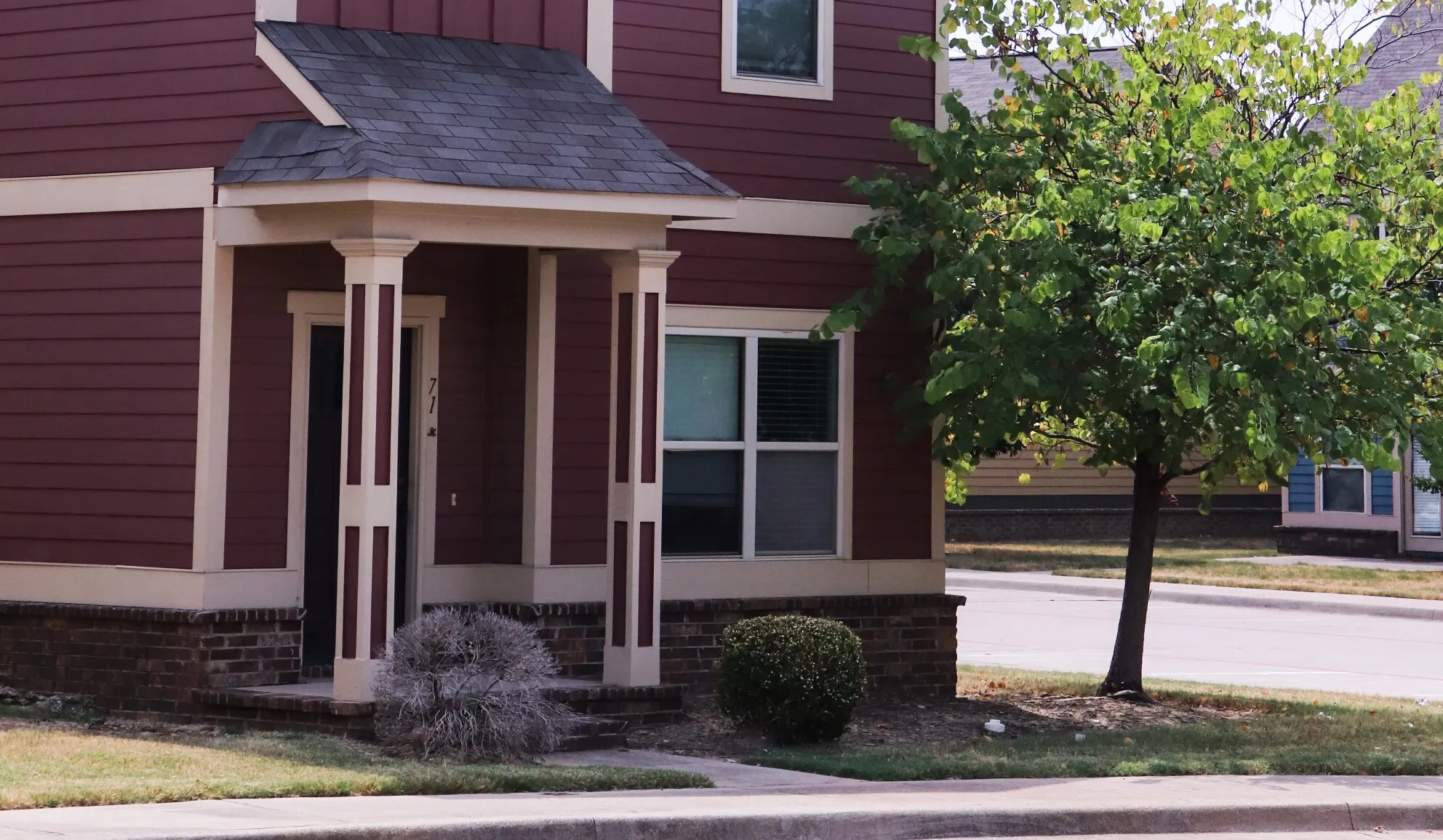 Exterior of townhome with red and cream siding during a sunny day.