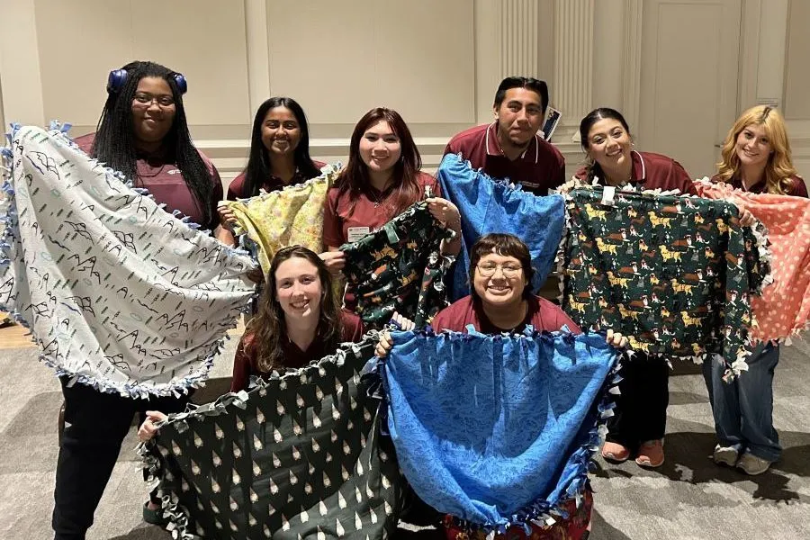 A group of students & staff pose with blankets they made.