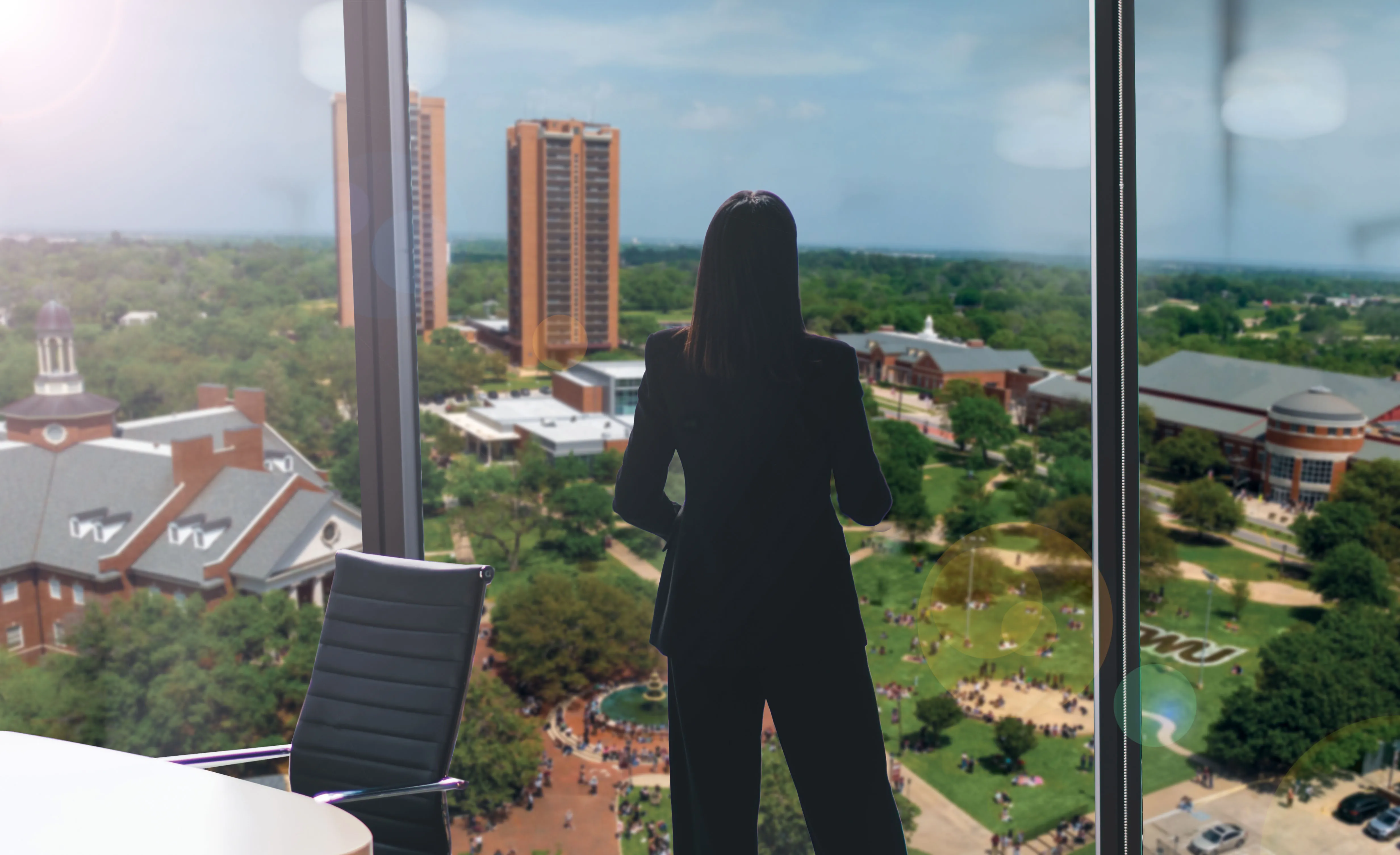 Woman overlooking the TWU campus from a tall building through a large window.  