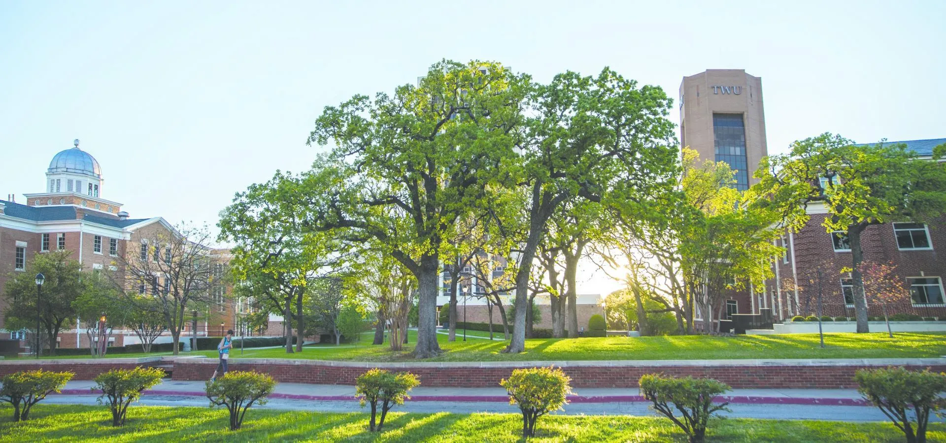 Depicts a sunny Spring morning on campus with the Old Main building on the left and the ACT tower on the right.  