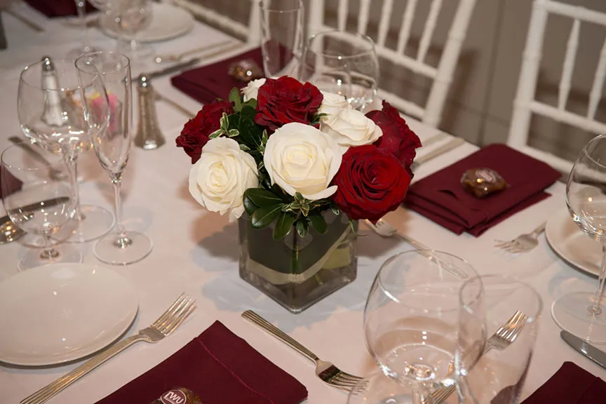 a vase with a group of red and white roses on a dinner table