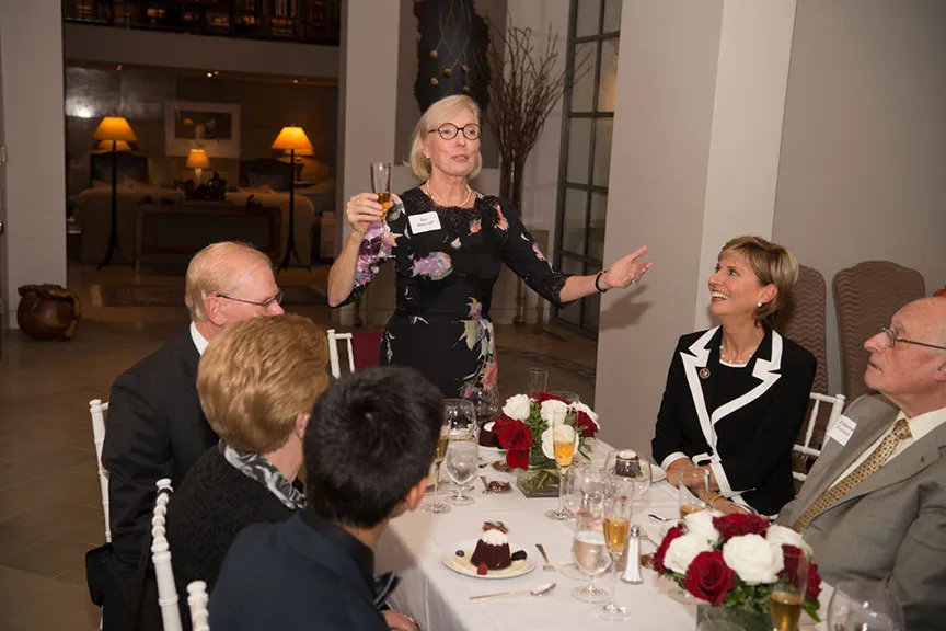 Sue Bancroft stands and proposes a toast at a dinner table with Chancellor Feyten