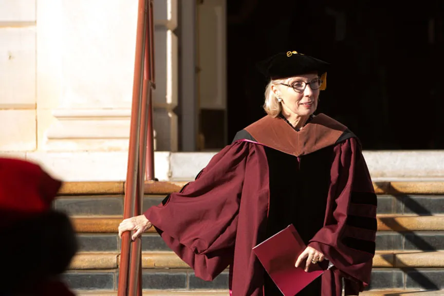 a woman in university regalia descends the steps of the Music building on Pioneer Circle