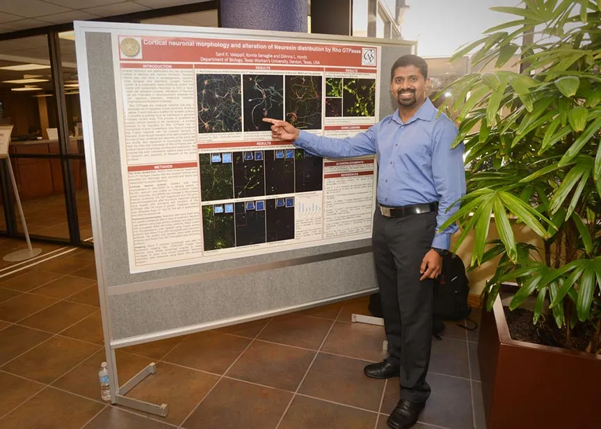 a man smiles and points to a scientific presentation poster